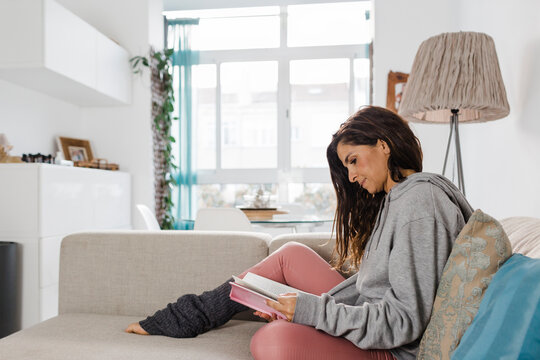 Mature woman reading book sitting on sofa in living room at home