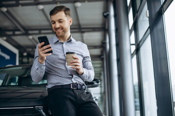 Customer in car salon drinking coffee and using phone