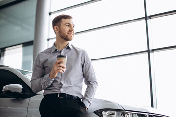 Customer in car salon drinking coffee and using phone
