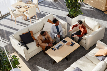 Young businessmen and businesswoman discussing strategy sitting on sofa in modern office