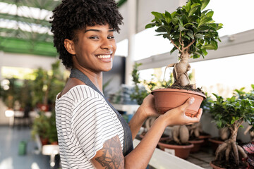 Happy gardener with curly hair holding Bonsai tree at nursery