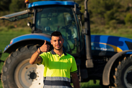 Young farmer gesturing thumbs up in front of tractor