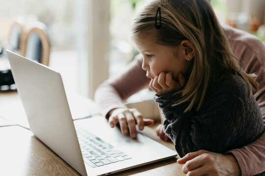 Girl with hand on chin looking at laptop sitting with mother
