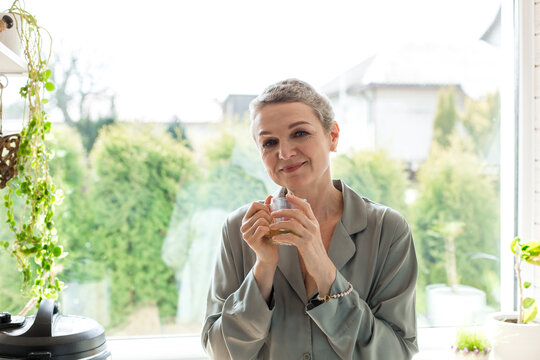 Mature woman holding tea glass at the window at home