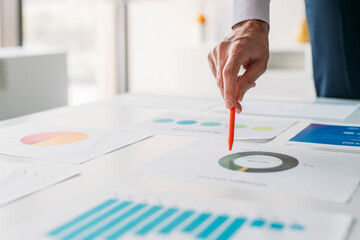 Hand of businessman with pen analyzing graphs and chart in office
