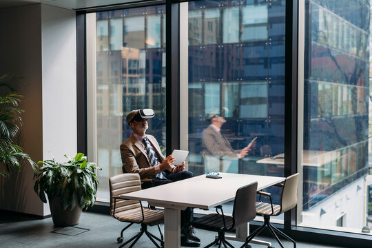 Businessman wearing virtual reality simulator sitting on chair by window in office
