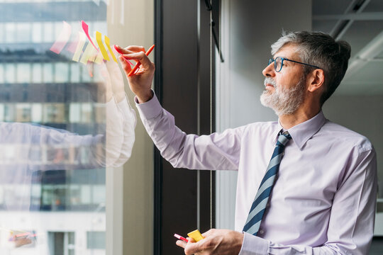 Businessman sticking adhesive notes on glass window in office
