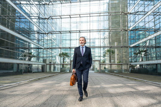 Businessman with bag walking in front of modern glass building