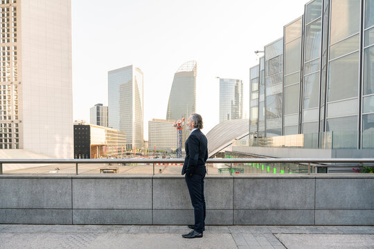 Mature businessman with hand in pocket standing by railing