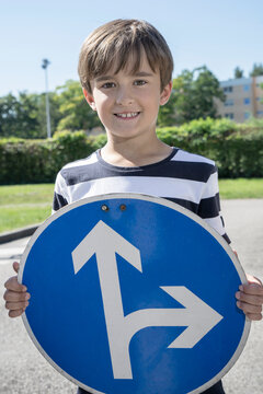 Smiling boy holding road sign board with arrow symbol on sunny day