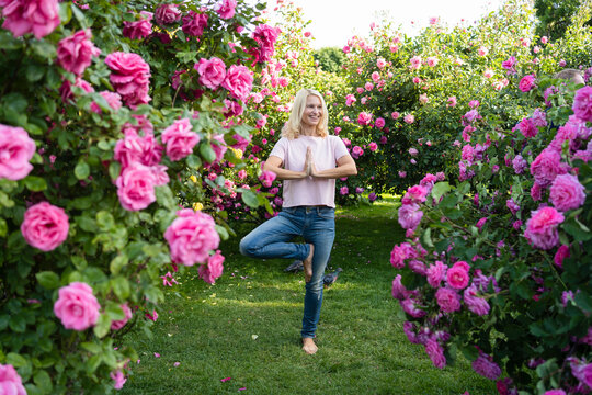 Happy Woman Doing Tree Pose Yoga Amidst Rose Garden