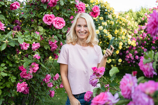Happy woman holding mobile phone amidst rose garden