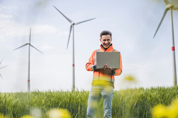 Happy engineer with laptop standing on field