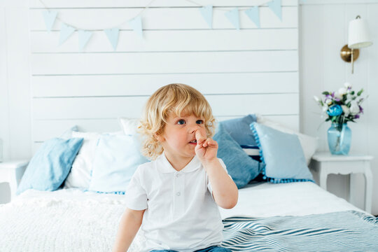 Boy picking nose sitting on bed at home