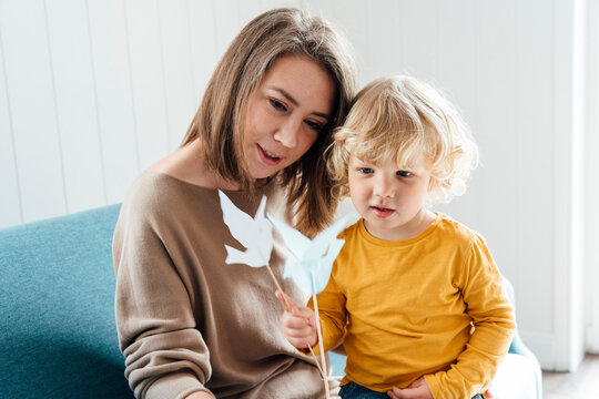 Mother with son holding origami birds sitting on sofa at home