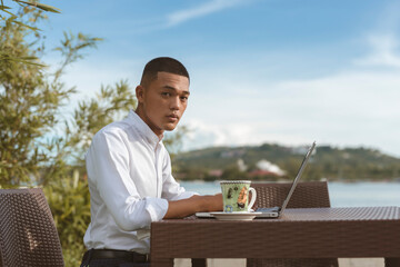A Filipino male data analyst working remotely at an outdoor cafe, coffee shop, or restaurant....