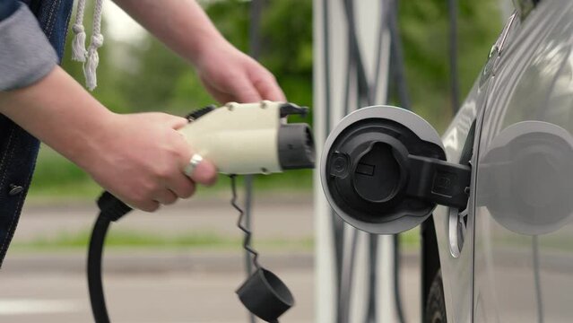 Unrecognizable man unplugs power connector into EV car. Male hand disconnects charging cable to electric vehicle, finish charge batteries. EV station in parking lot