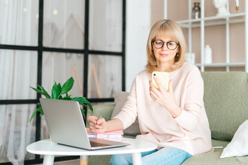 Cute adult senior mature woman in glasses checking text messages in her smartphone cell phone...