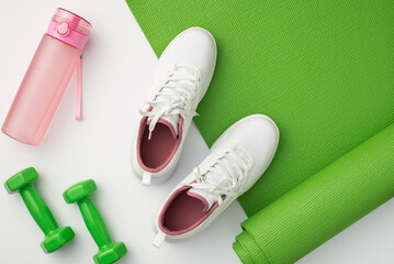 Fitness concept. Top view photo of white sneakers pink bottle of water green exercise mat and...
