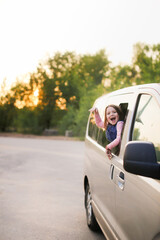 Funny European kid girl peeking out of window of minivan, family trips with children