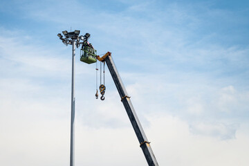 Electrician repairing lighting on tall columns with a lift crane.