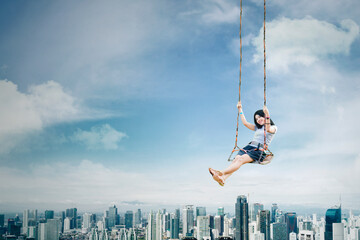 Happy woman sitting on the swing above the city - obrazy, fototapety, plakaty
