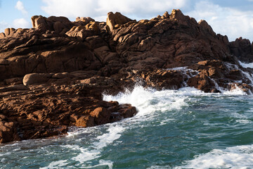 Rising tide and big waves hit rocky coast in sunlight in northern France.