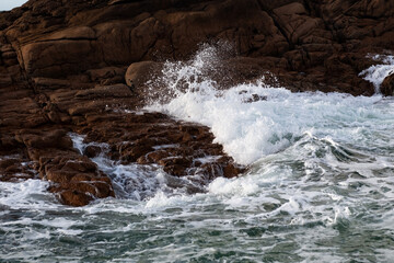 Rising tide and big waves hit rocky coast in sunlight in northern France.