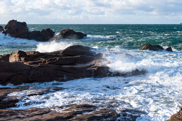 Rough sea and big waves hit rocks under friendly sky.