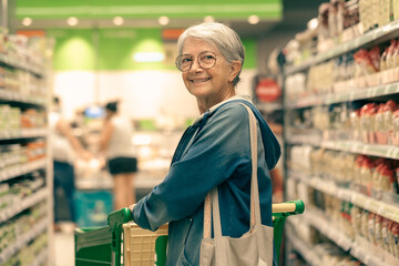 Portrait smiling senior woman making purchases in the supermarket pushing shopping cart. Caucasian...