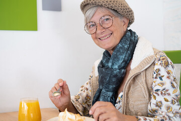 Beautiful caucasian senior woman sitting for breakfast in cafe, smiling female eating a lemon cake...
