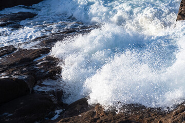 Rough sea and big waves hit rocks creating enormous spray.