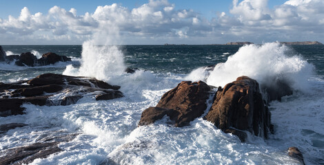 Rough sea and big waves hit rocks under friendly sky.