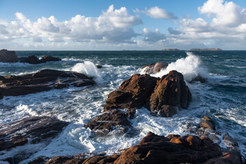 Rough sea and big waves hit rocks under friendly sky.