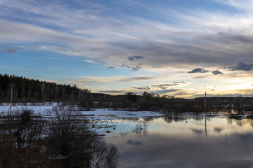 Epic spring landscape by the river. The flood of the river in early spring. A colorful sunset is reflected in the water. March evening landscape.