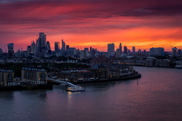The illuminated london skyline with river Thames and skyscrapers during a fiery summer sunset, England