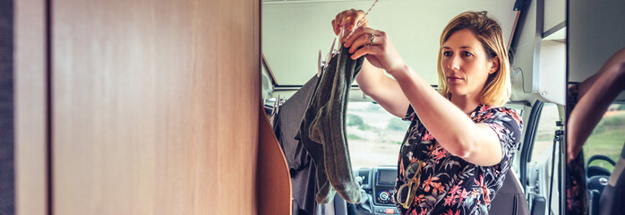 Young woman hanging clothes on a rope inside her camper van during a trip
