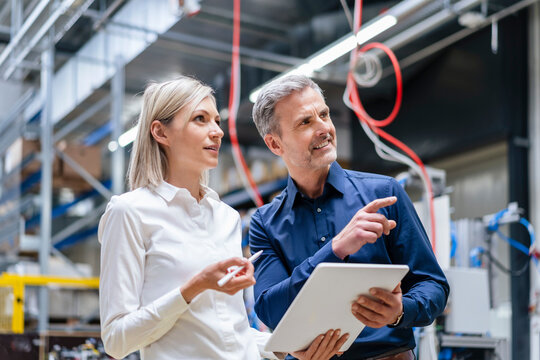 Businessman and businesswoman with digital tablet talking in factory - Powered by Adobe