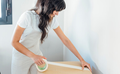 Woman with adhesive tape packing cardboard box at home