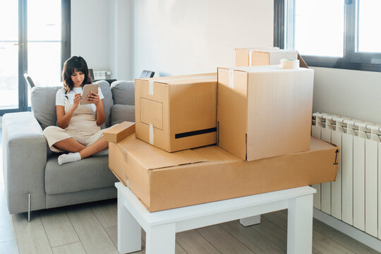 Woman using tablet PC sitting on sofa in living room at new home