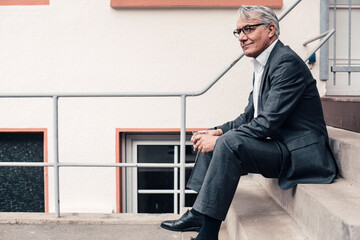 Contemplative senior businessman sitting on steps outside building