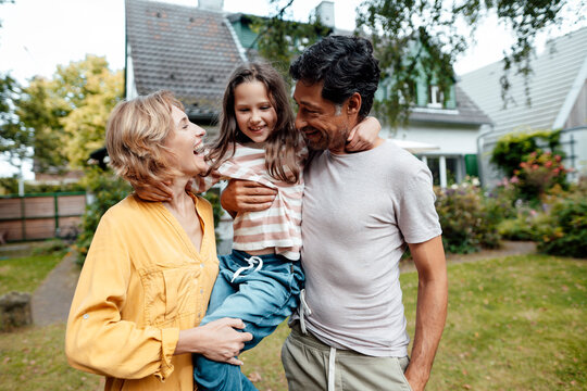 Happy parents carrying daughter in front of house - Powered by Adobe