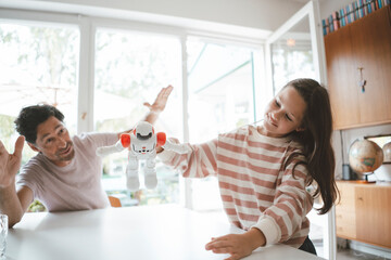 Girl playing with toy robot by father sitting at table