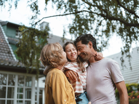 Happy parents embracing daughter standing in front of house