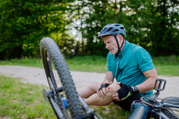 Fototapeta Active senior man in sportswear fell off bicycle on the ground and injured his knee, in park in summer. obraz