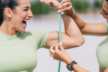 Happy woman measuring sister's bicep on sunny day