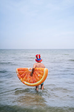 Man carrying inflatable orange slice walking in sea
