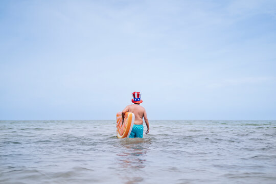 Shirtless man walking in sea carrying inflatable orange slice