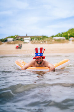 Smiling man wearing Uncle Sam hat swimming with pool raft in sea