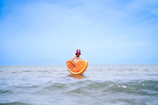 Man carrying inflatable orange slice standing in sea